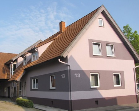 Violette Fassade eines Hauses mit dunklen Rechtecken um die Fenster gestaltet